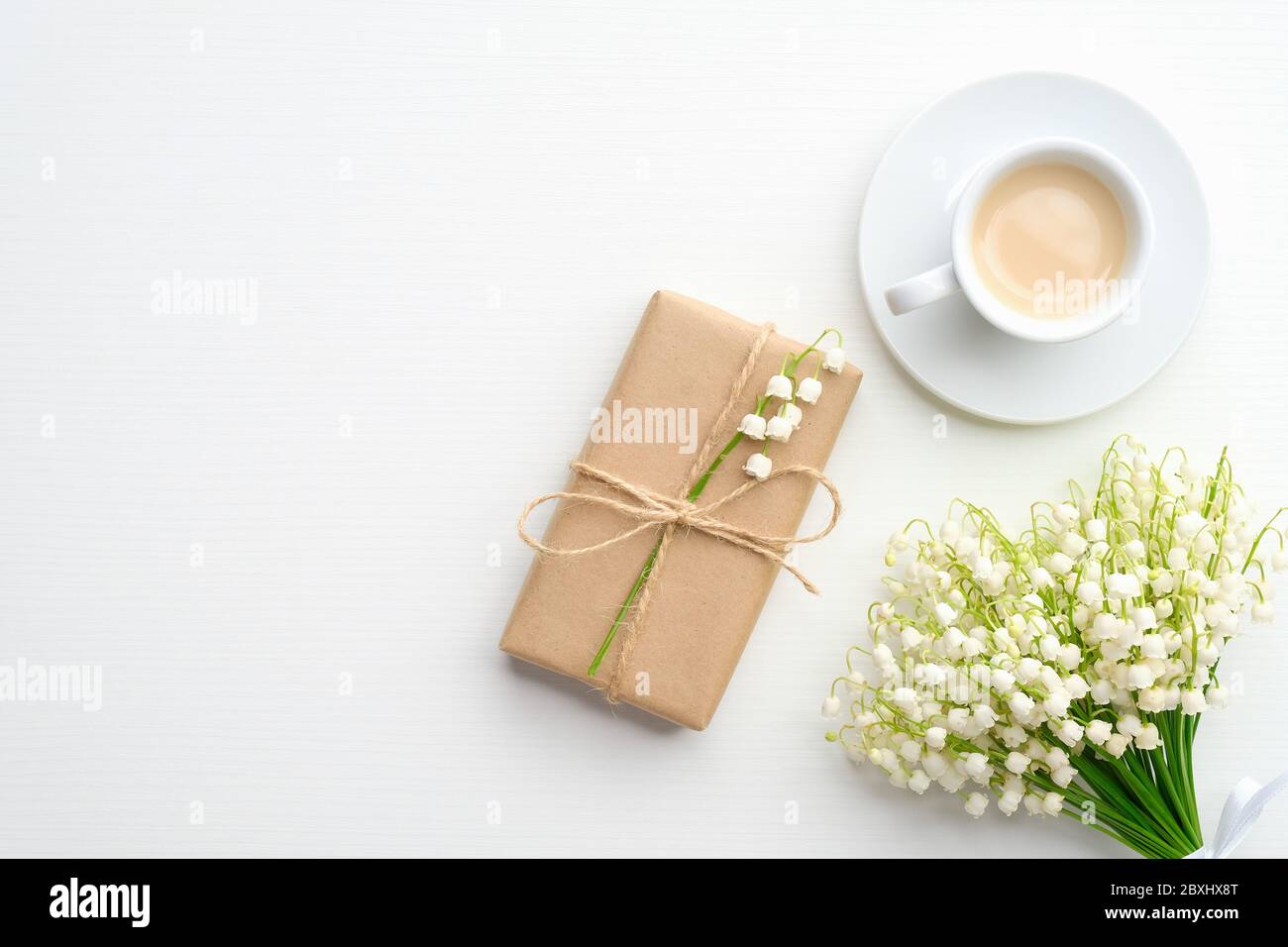 Boîte cadeau de mariage, bouquet de fleurs de la vallée, tasse de café sur fond blanc. Flat lay, vue de dessus. Banque D'Images