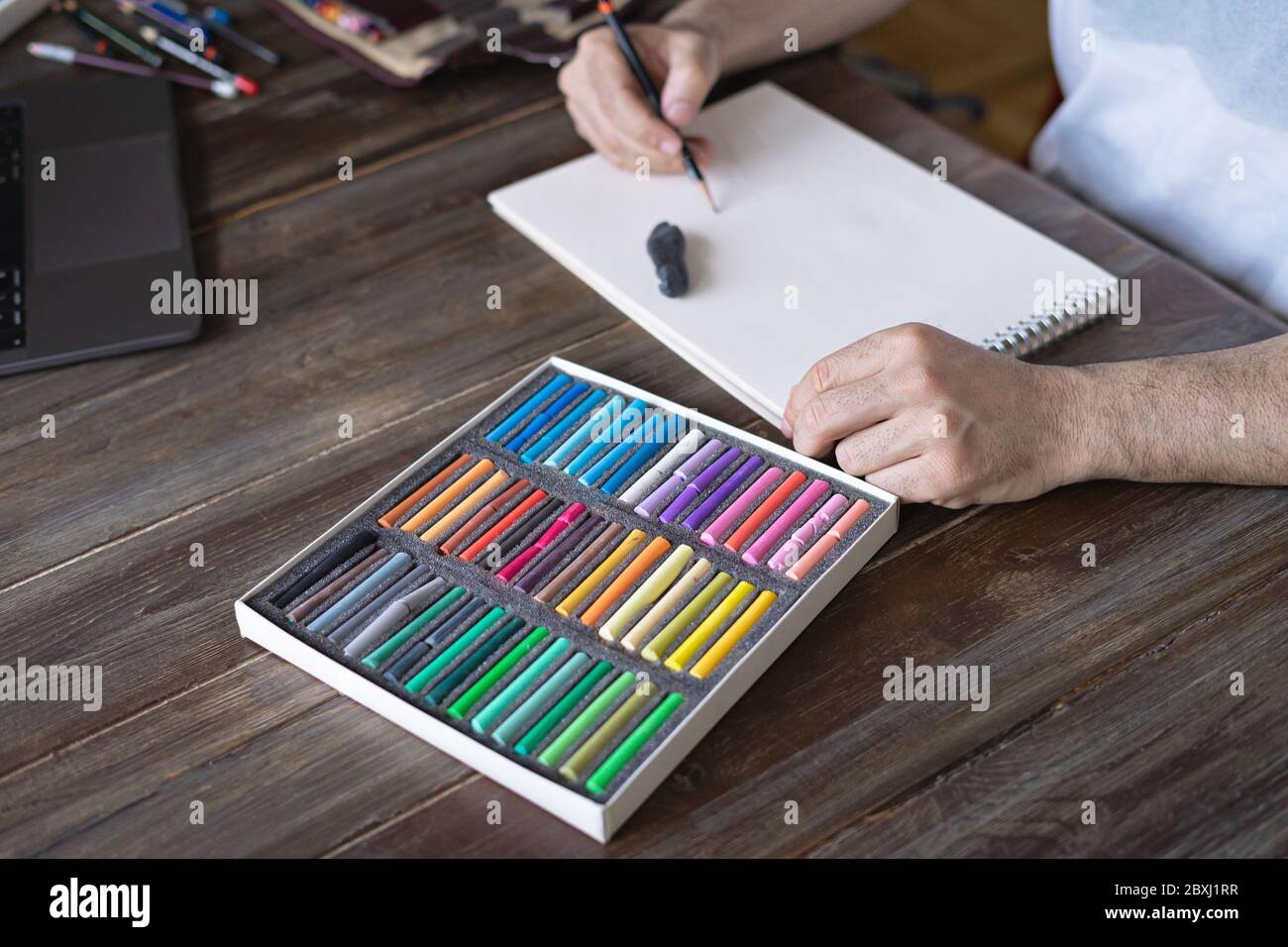 personne peignant avec une craie pastel sur un papier blanc avec une pallette de craies pastel sur la table en bois Banque D'Images