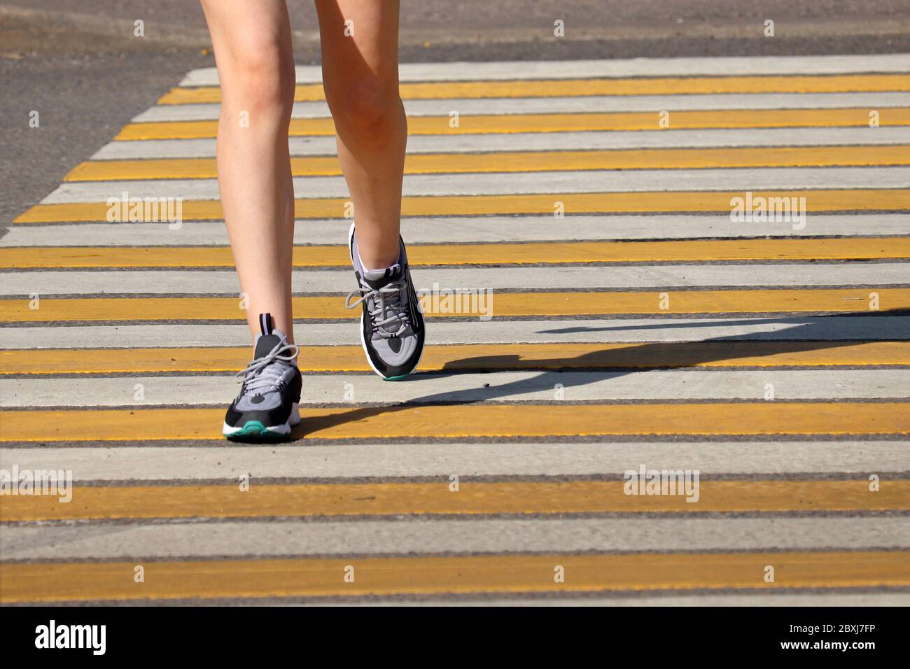 Petite fille traversant la rue, jambes de femme dans les baskets sur le passage piéton. Concept de sécurité routière, femme en course à pied dans la ville d'été Banque D'Images