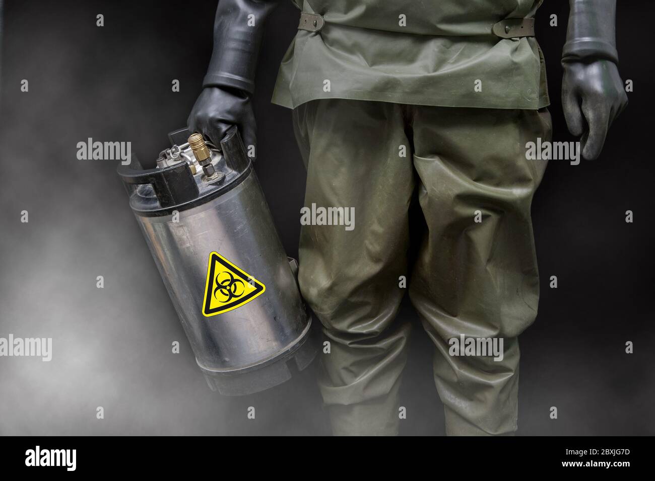 Un homme en costume de protection NBC tient un contenant en métal spécial dans sa main avec un autocollant d'avertissement de danger biologique. Banque D'Images