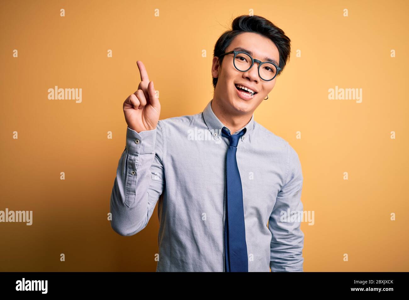 Jeune homme d'affaires chinois élégant portant des lunettes et cravate sur  fond jaune montrant et pointant vers le haut avec le doigt numéro un tout  en souriant confide Photo Stock - Alamy