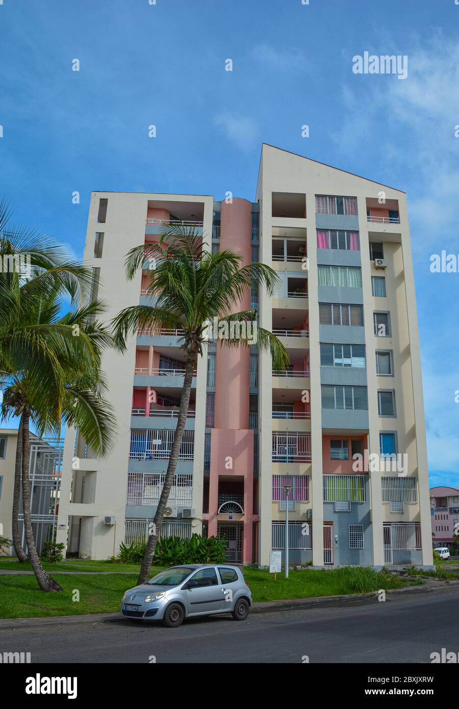 Point-a-Pitre, Guadeloupe - 17 septembre 2018 : immeuble résidentiel coloré de gens du coin sur la rue avec des palmiers verts, route et une voiture garée Banque D'Images