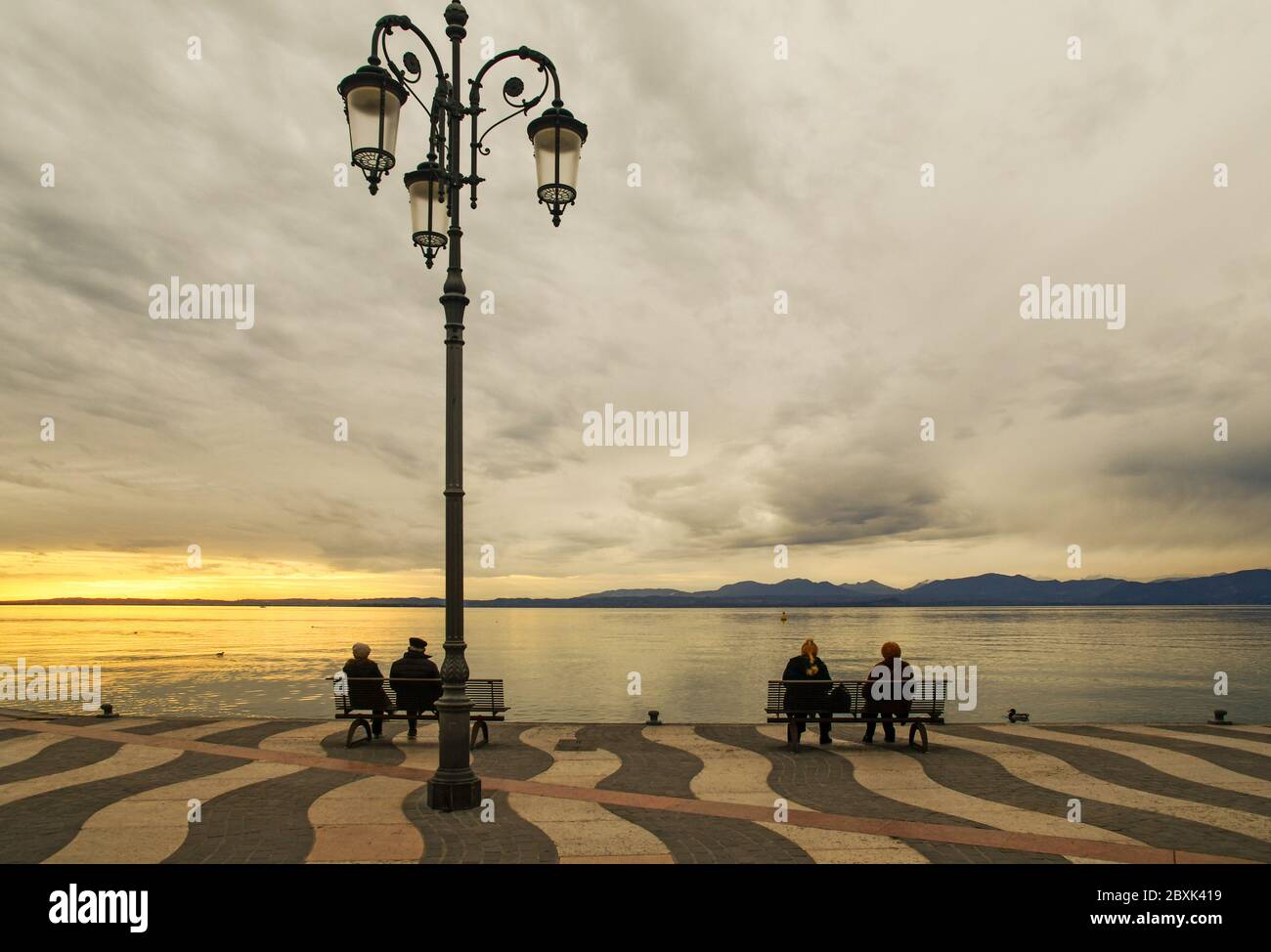 Vue panoramique sur la rive du lac de Garde avec des personnes assises sur des bancs sur la promenade au coucher du soleil, Lazise, Vérone, Vénétie, Italie Banque D'Images