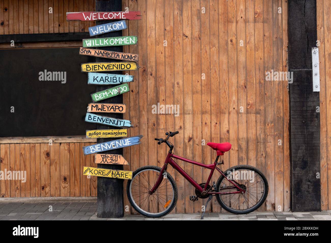 Vélo rouge stationné à côté d'un poteau avec des panneaux de bienvenue dans plusieurs langues différentes. Banque D'Images