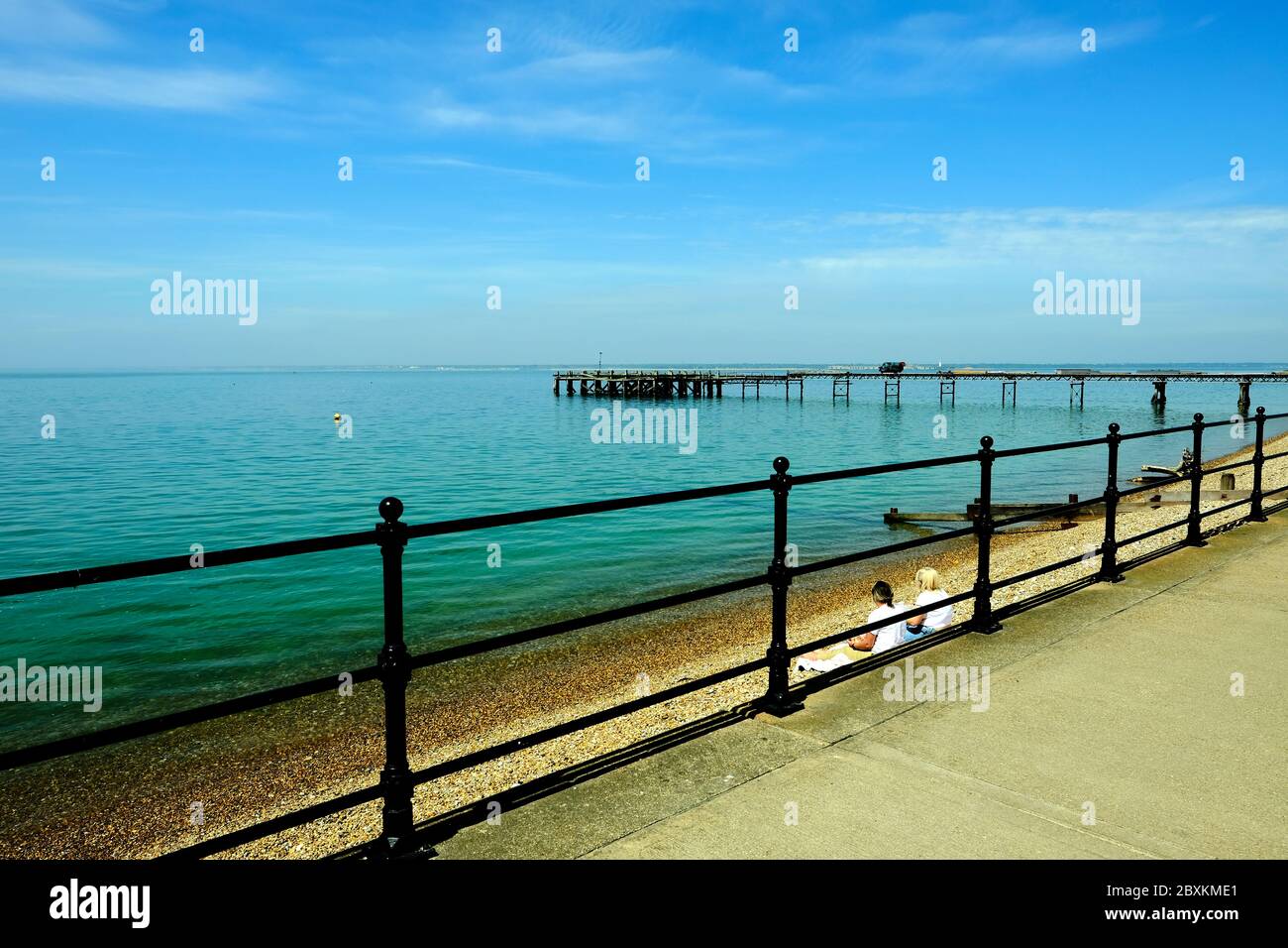 Totland Bay, front de mer, île de Wight, montrant l'ancien victorien jetée de l'autre côté du Solent vers la partie continentale deux femmes assises sur la plage Banque D'Images