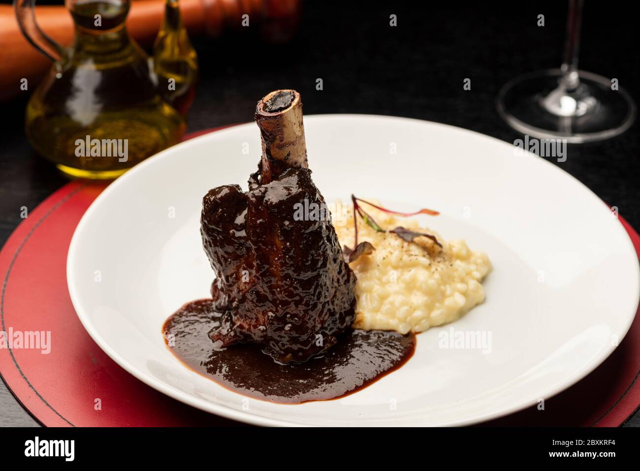 Jarret d'agneau braisé, Stinco di agnello vitello brasato avec sauce et risotto sur fond noir flou avec moulin à poivre et huile d'olive Banque D'Images