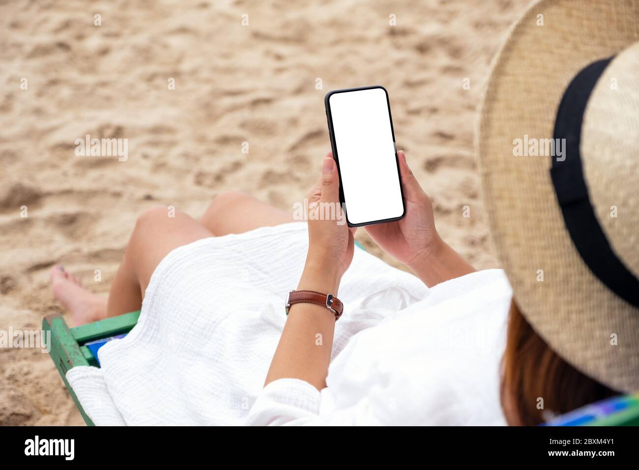 Image d'une femme tenant un téléphone portable noir avec un écran de bureau vierge tout en étant allongé sur une chaise de plage Banque D'Images