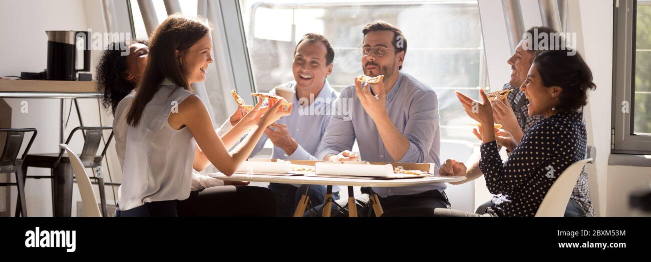 Le personnel multiethnique s'est réuni dans la cuisine du bureau en riant avec de la pizza Banque D'Images