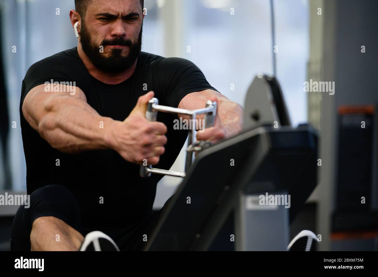 entraînement intensif sport entraînement en salle de gym par un jeune homme barbu fort tirant un poids lourd assis sur l'équipement de fitness Banque D'Images