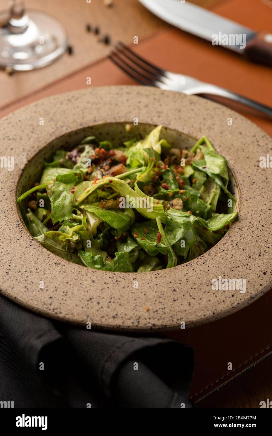 salade césar avec bacon aux noix caramélisées sur un bol en céramique, un verre à vin et un tapis en cuir Banque D'Images
