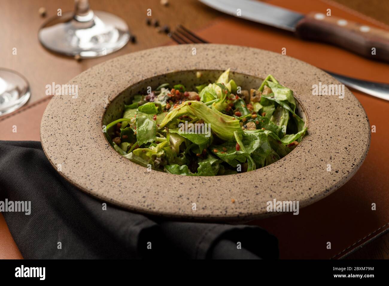 salade césar avec bacon aux noix caramélisées sur un bol en céramique, un verre à vin et un tapis en cuir Banque D'Images