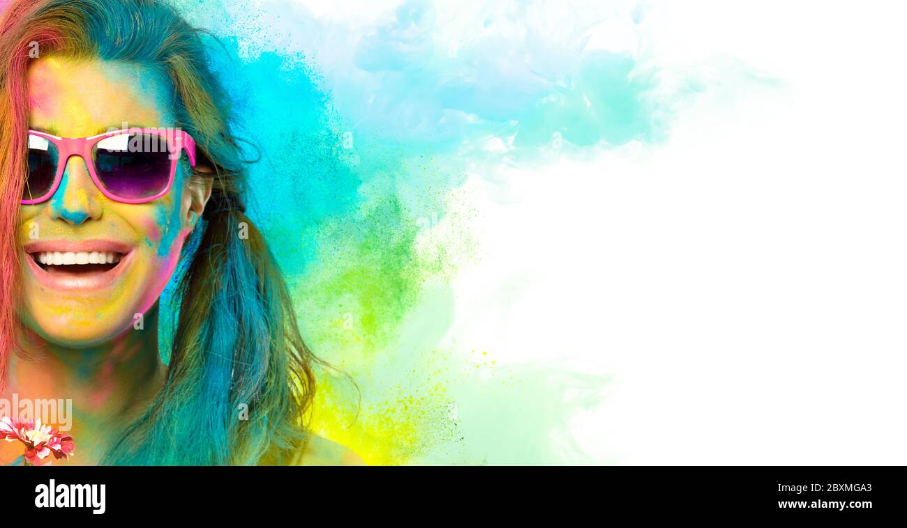 Belle jeune femme joyeuse célébrant le festival Holi des couleurs, recouverte de poudre de couleur arc-en-ciel avec des lunettes de soleil roses souriantes à l'appareil photo. Magnifique p Banque D'Images