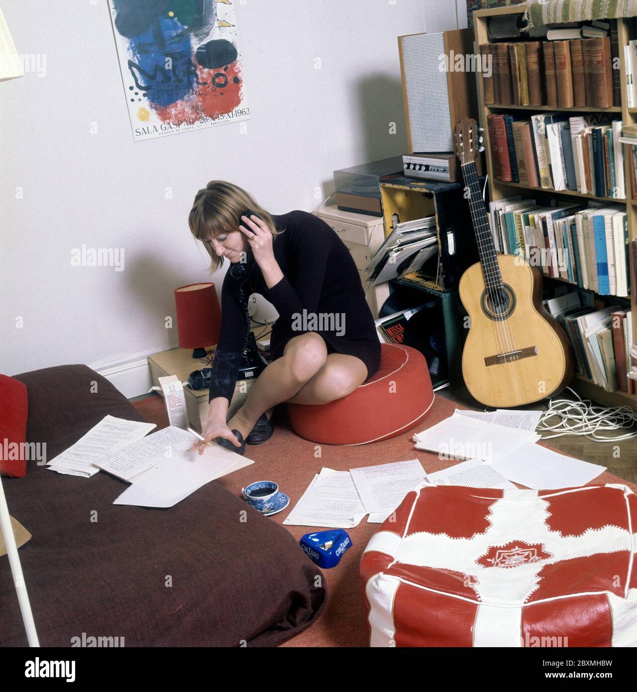 Dans les années 1960. Une jeune femme dans son appartement. Un étudiant à la maison avec une bibliothèque pleine de livres et de littérature. Tout en parlant au téléphone et en fume une cigarette, elle a un regard sur certains documents qui sont étalées sur le sol et le lit. Photo prise en novembre 21 1968. Kristoffersson réf. CV51-1 Banque D'Images