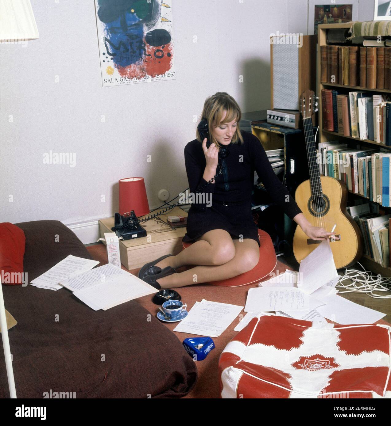 Dans les années 1960. Une jeune femme dans son appartement. Un étudiant à la maison avec une bibliothèque pleine de livres et de littérature. Tout en parlant au téléphone et en fume une cigarette, elle a un regard sur certains documents qui sont étalées sur le sol et le lit. Photo prise en novembre 21 1968. Kristoffersson réf. CV51-3 Banque D'Images
