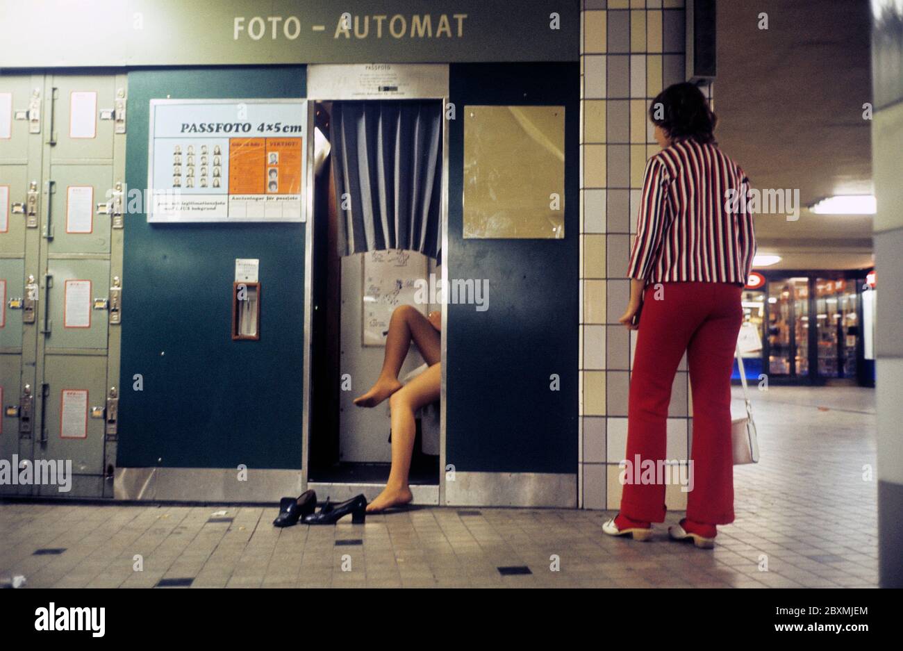 Dans les années 1970. Un stand de photo à une station de métro qui par l'apparence de lui est utilisé pour d'autres photos puis les photos de passeport usuelles. Une femme est debout regardant la personne à l'intérieur qui a enlevé ses chaussures et est assise à l'intérieur de façon décontractée la prise de sa photo. Suède 1971. Réf. CV48-5 Banque D'Images
