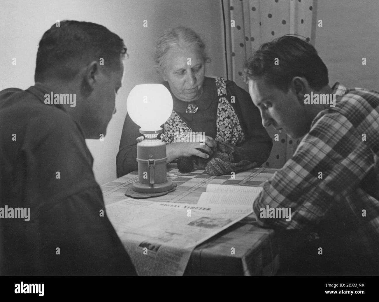 Dans les années 1940. Une femme âgée et deux jeunes hommes trient et lisent à la lumière d'une lampe en carbure. Lampe qui produit et brûle l'acétylène, créée par la réaction chimique du carbure de calcium et de l'eau. Suède 1942 Banque D'Images