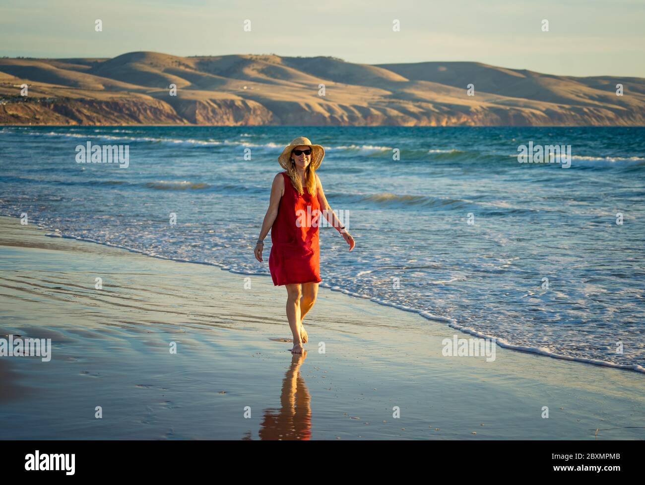Heureuse femme mature attrayante en robe rouge appréciant l'extérieur et la liberté sur la plage, les bras ouverts s'étirent dans l'espoir après la quarantaine du coronavirus eas Banque D'Images