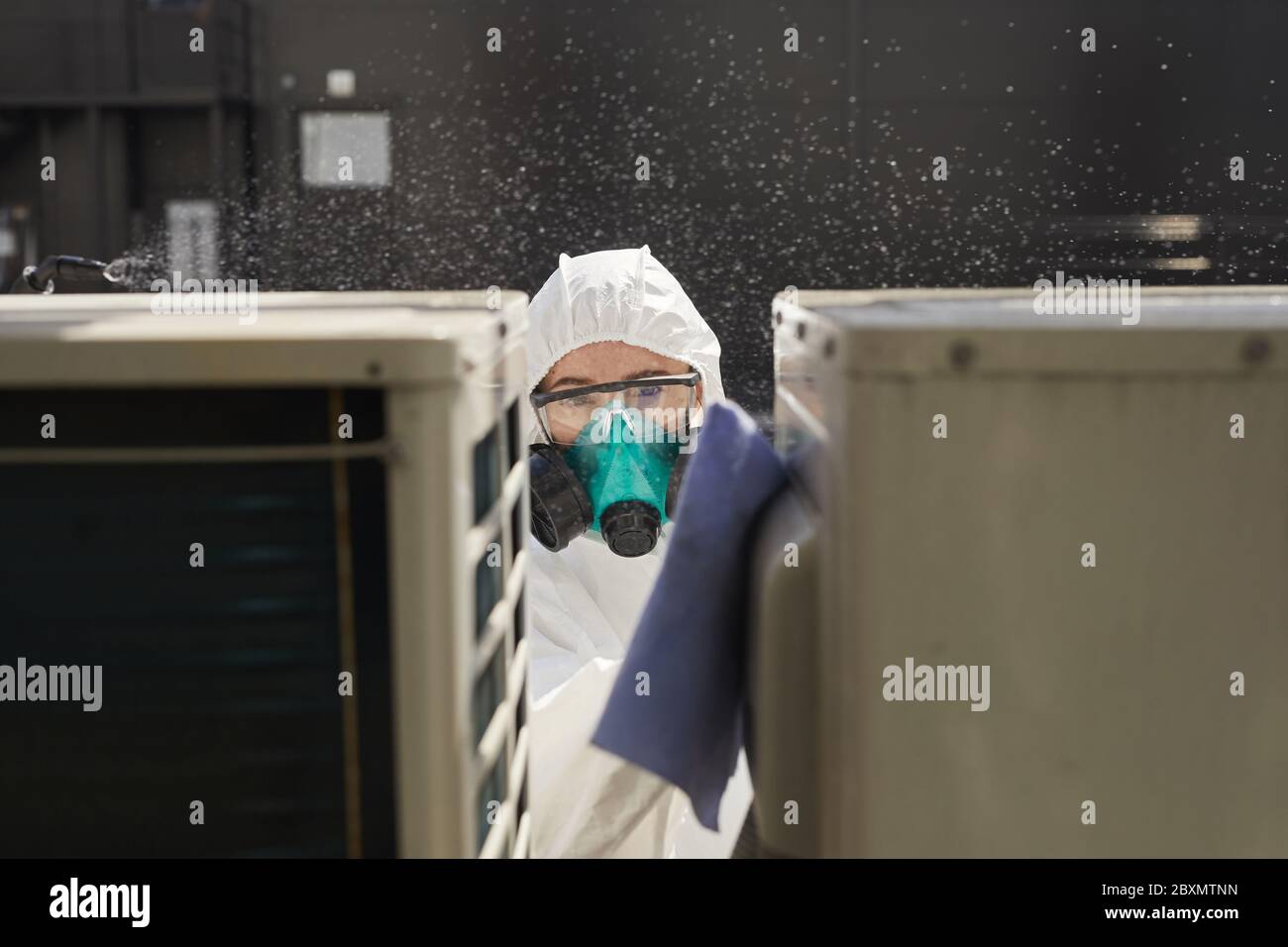 Portrait d'une femme travaillant avec un vêtement de protection et désinfectant les surfaces d'un respirateur à l'extérieur éclairé par la lumière du soleil, espace de copie Banque D'Images