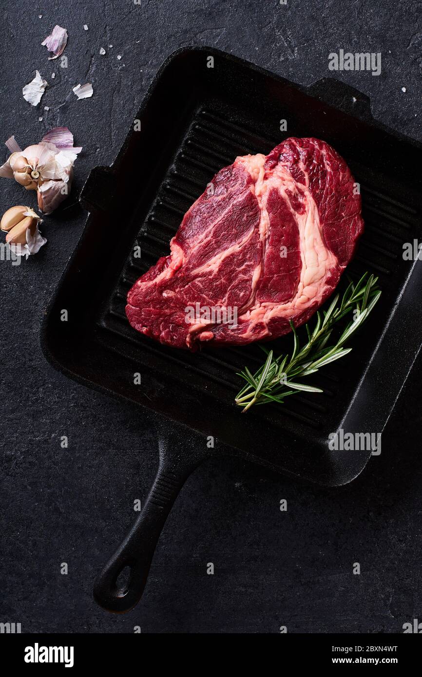 Vue du haut Black Angus Prime Beef Chuck roulé steak sur une poêle à frire en fonte avec romarin frais, thym, huile d'olive, ail et épices. Mise en page créative Banque D'Images