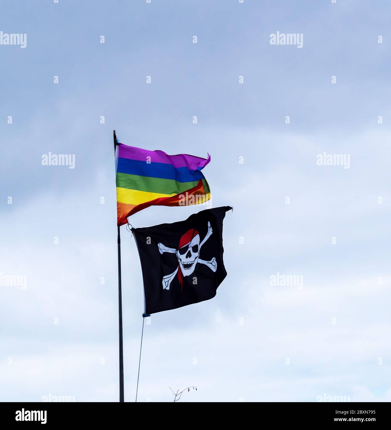 Drapeaux. Jolly Roger aka crâne et Crossbone, et arc-en-ciel. Contre le ciel, juxtaposition inhabituelle. Banque D'Images