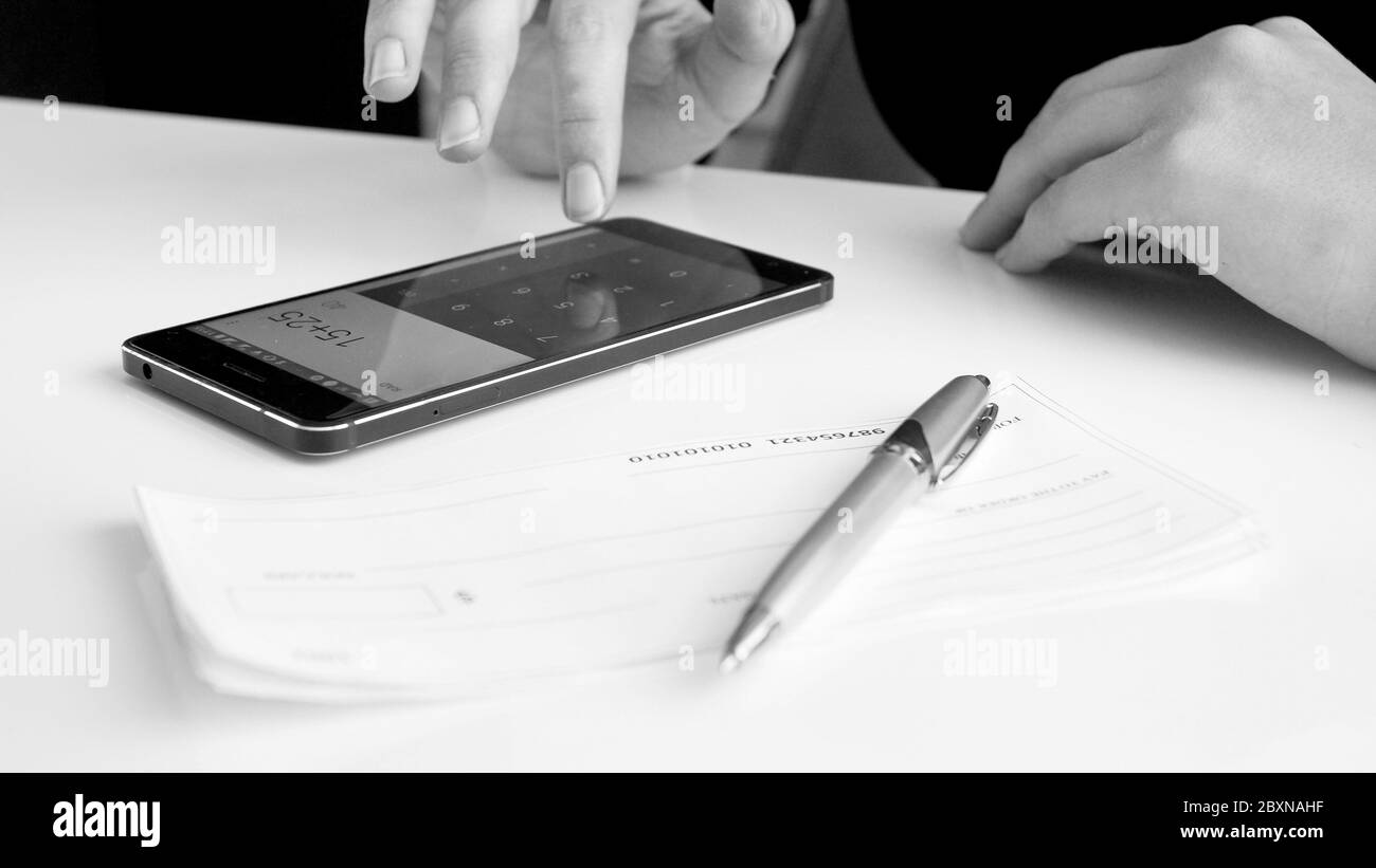 Image en noir et blanc de la femme effectuant un calcul financier sur smartphone avant de signer le chèque bancaire Banque D'Images