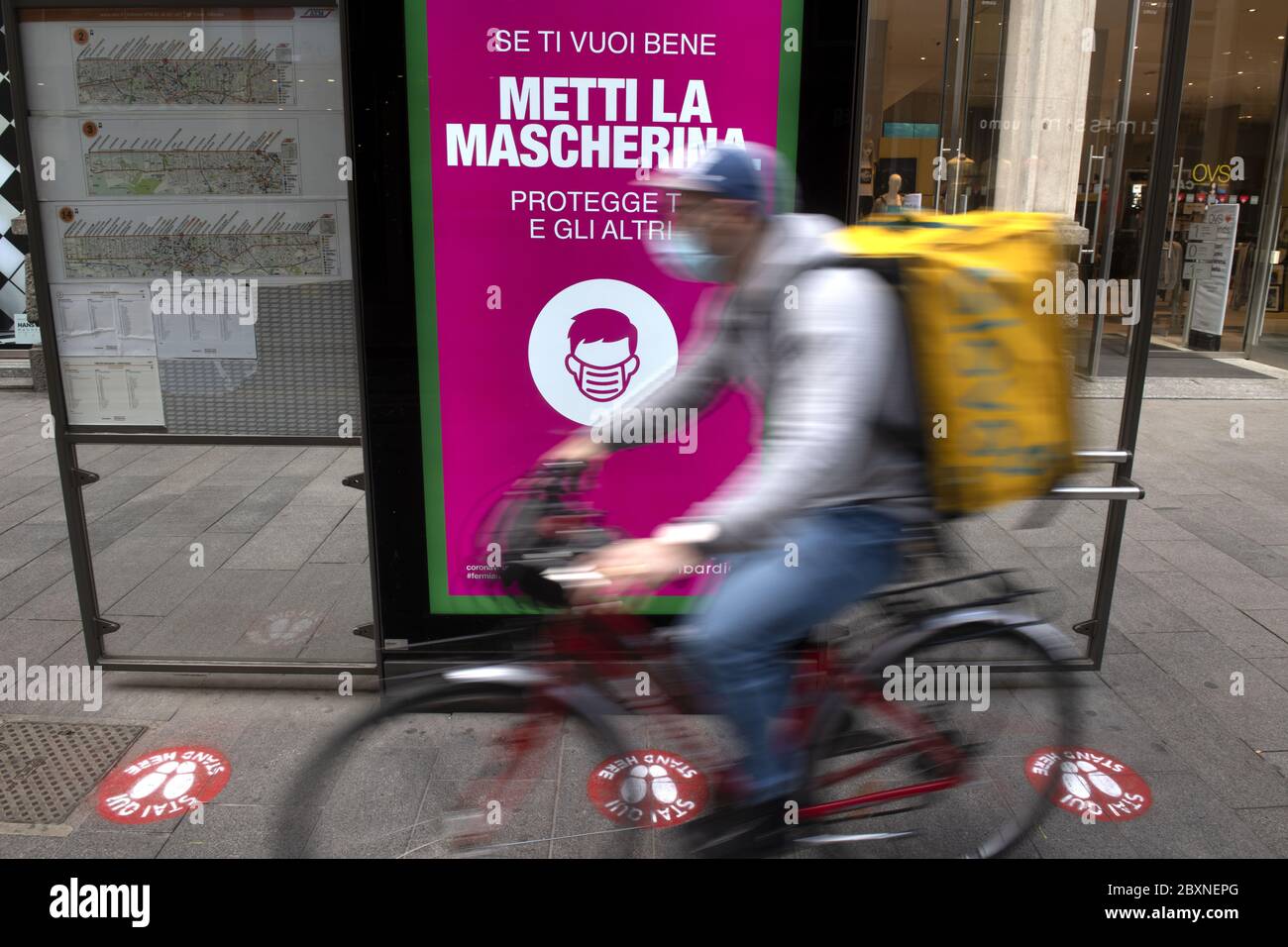 Un motard de livraison passe par une station de tramway avec des panneaux de distance sociale sur le sol pour la sécurité sanitaire pendant le Covid-19 à Milan, Italie. Banque D'Images