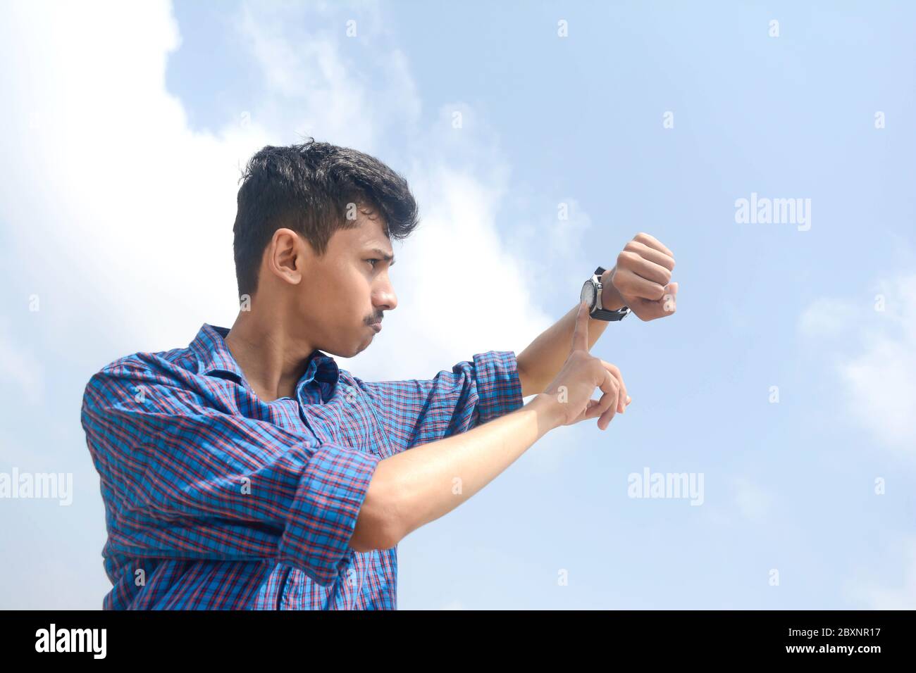 Portrait d'un jeune homme regardant sa montre. Isolé sur fond de ciel. Banque D'Images
