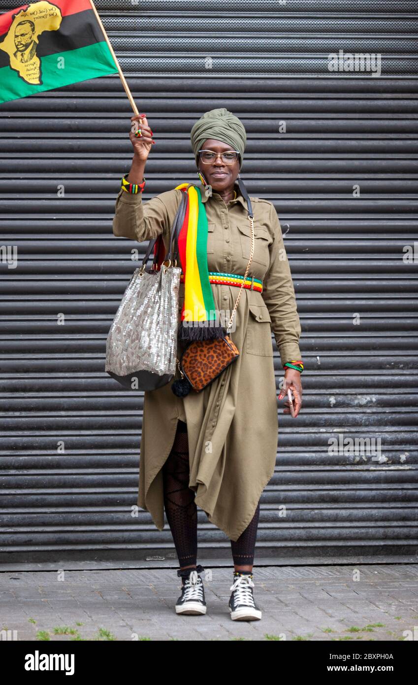 Portrait d'une femme d'âge moyen, debout devant un volet de sécurité en métal, portant des vêtements de fierté africaine et portant un drapeau. Londres, Royaume-Uni Banque D'Images