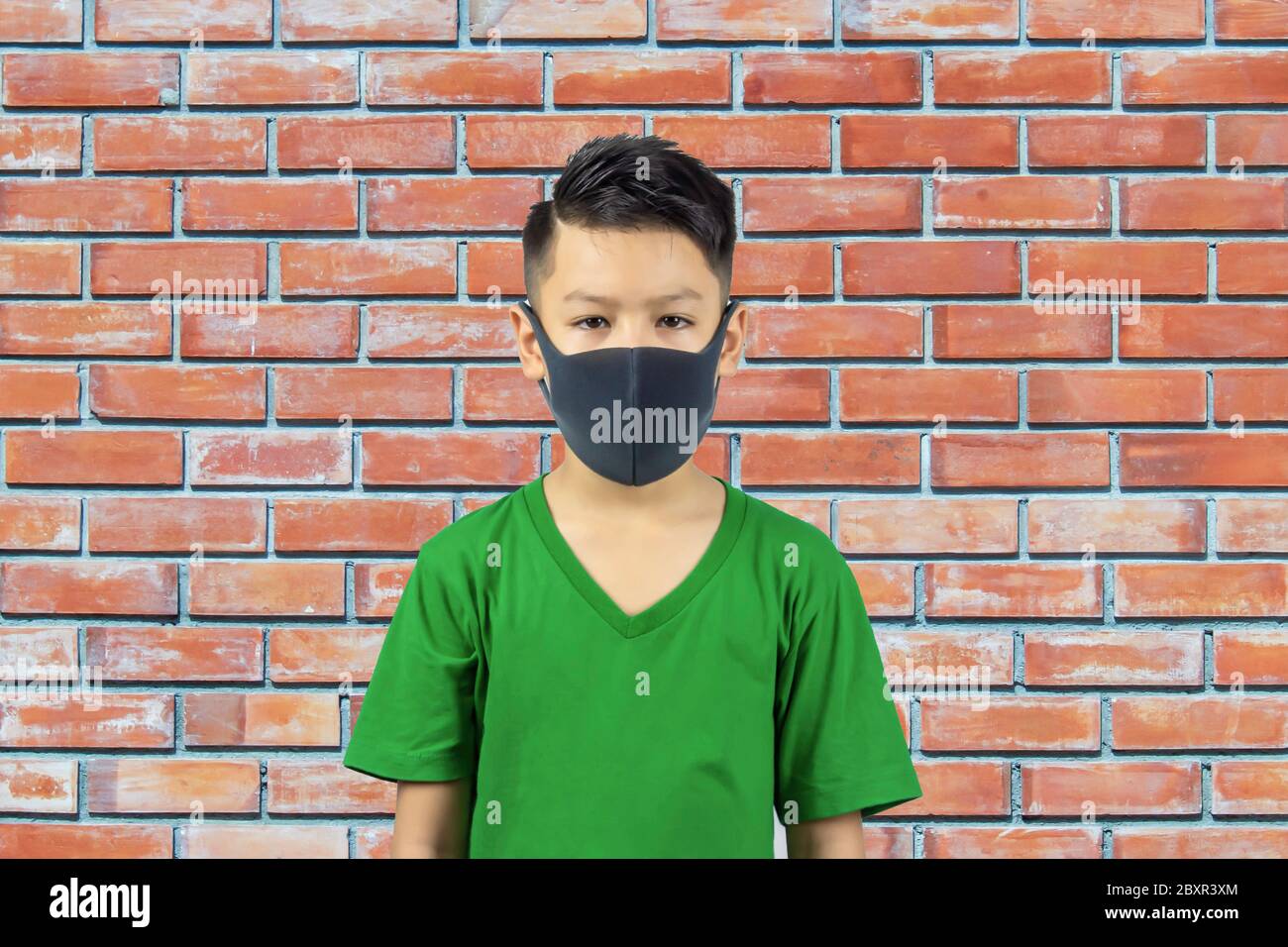 Portrait asiatique garçon portant un masque arrière-plan mur de brique. Banque D'Images