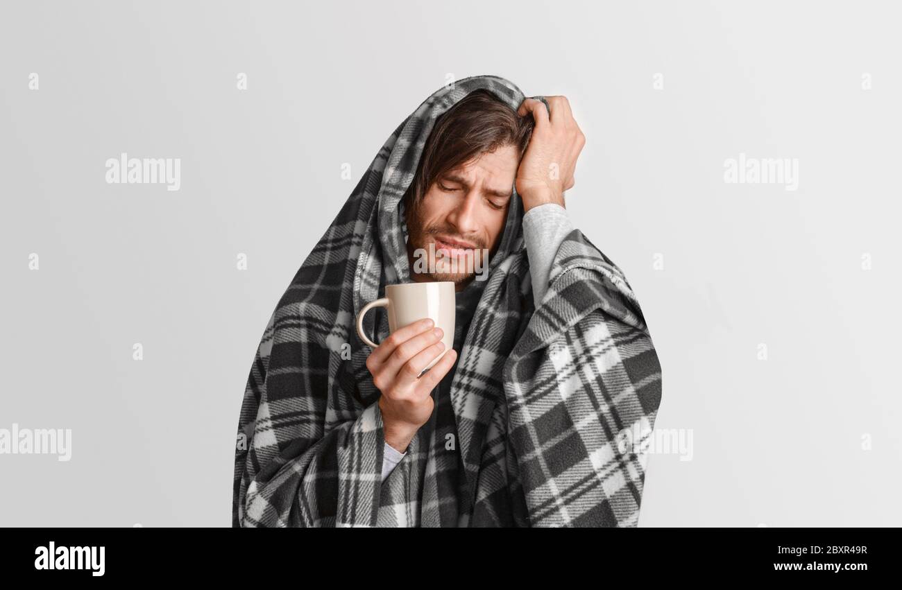 Traiter la grippe et le rhume. L'homme souffrant tient une tasse de boisson chaude et appuie sa main sur la tête Banque D'Images