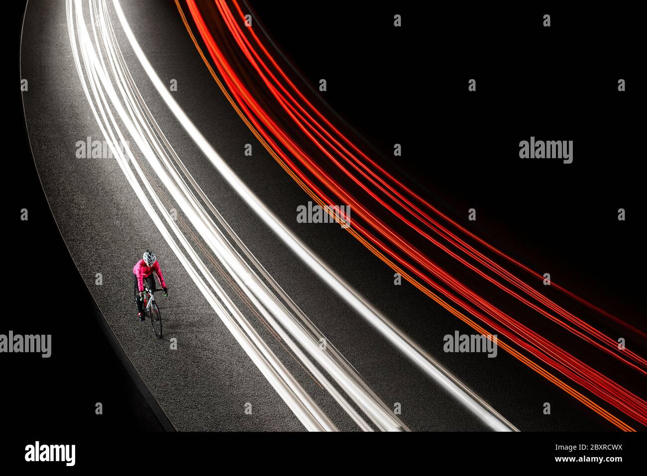Femme cycliste en blouson rose vif à vélo sur la route de nuit avec des pistes de lumière de voitures. Concept de mode de vie sain et de sport actif urbain. Banque D'Images