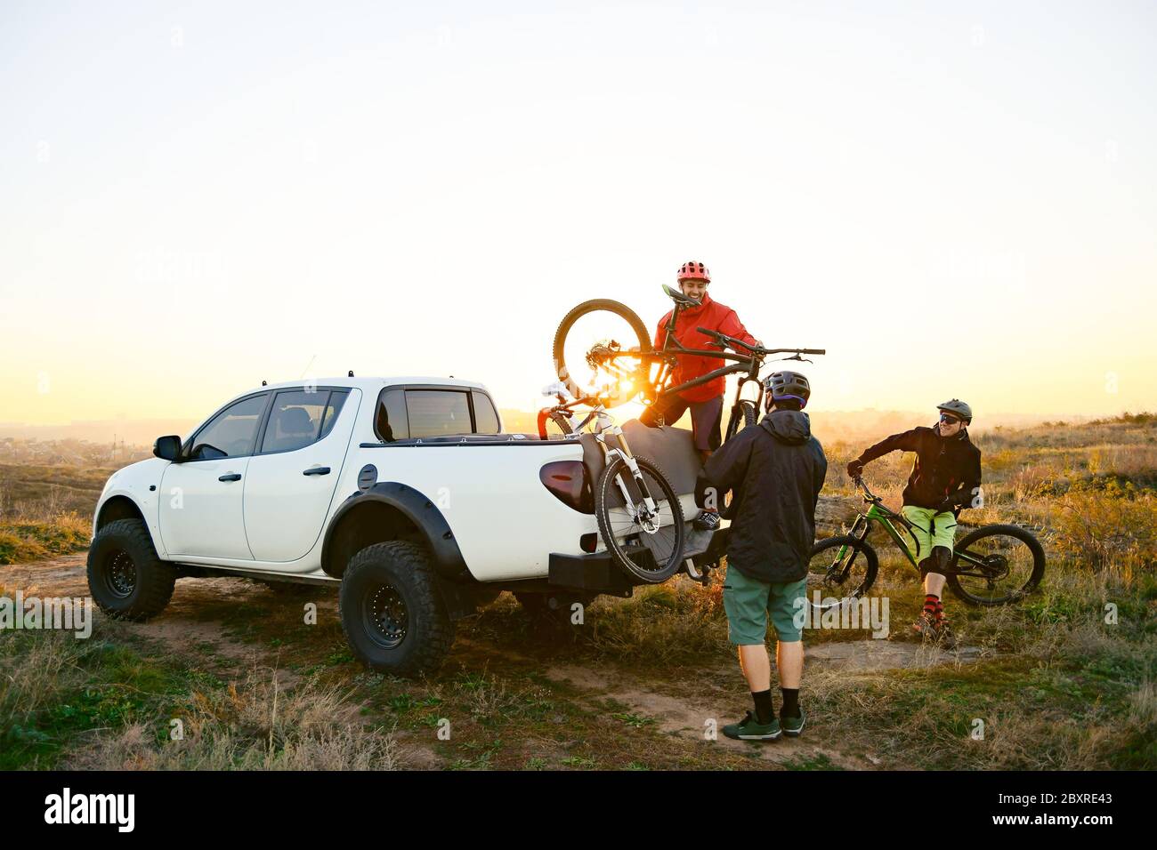 Amis cyclistes se préparer pour la randonnée à vélo et de prendre les vélos  du pick-up Offroad camion dans les montagnes à l'automne chaud coucher de  soleil. MTB Avent Photo Stock -