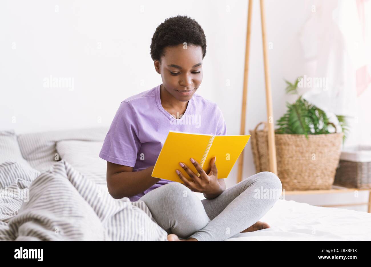 Travailler avec des notes. Femme lisant le bloc-notes, assise sur le lit dans la chambre à coucher intérieure Banque D'Images