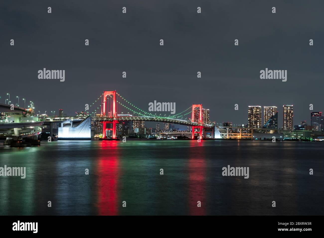 Vue nocturne du pont Rainbow, illuminé en rouge comme un signe de 'Tokyo Alert (alerte de coronavirus pour la région de Tokyo)' à Odaiba, Japon. Banque D'Images