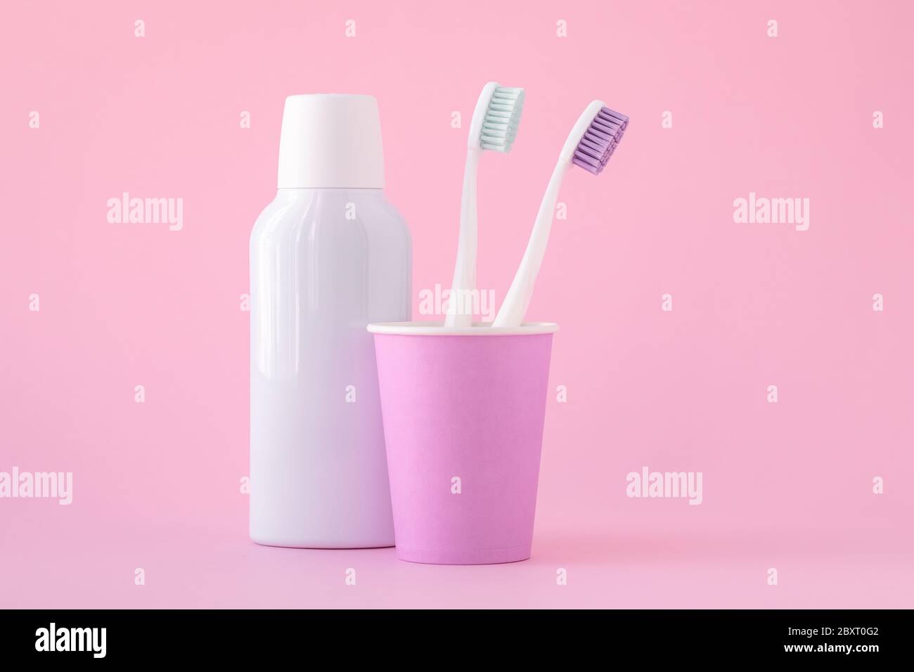 Deux brosses à dents blanches dans une tasse rose et un bain de bouche cosmétique dans une bouteille. Prévention des maladies dentaires et de la mauvaise haleine. Hygiène buccale, hygiène dentaire conce Banque D'Images