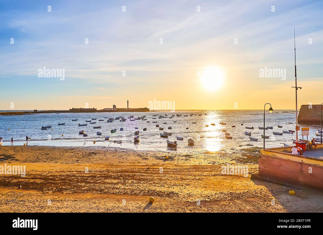 Le coucher du soleil avec de nombreux bateaux de pêche, amarrés à la plage de la Caleta avec une vue sur le château de San Sebastian à l'horizon, Cadix, Espagne Banque D'Images