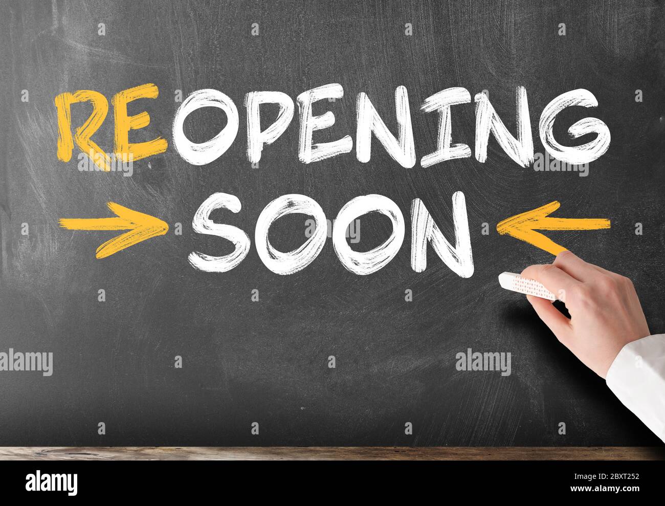 Main tenant un morceau de craie contre le tableau noir avec le texte ROUVRANT BIENTÔT Banque D'Images