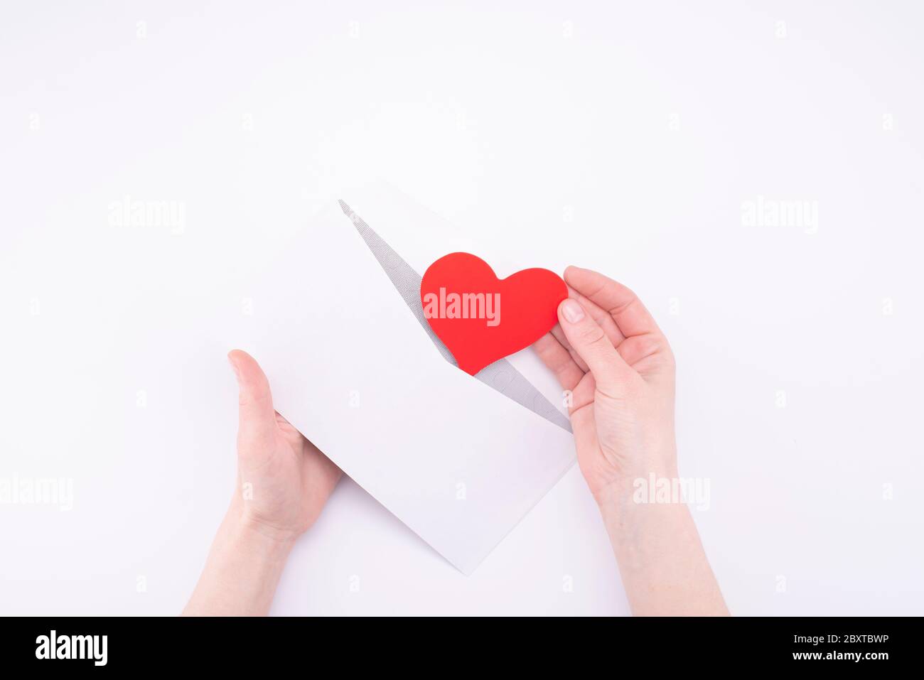 Mains retirer coeur Valentin de l'enveloppe blanche sur fond blanc. déclaration d'amour concept Banque D'Images