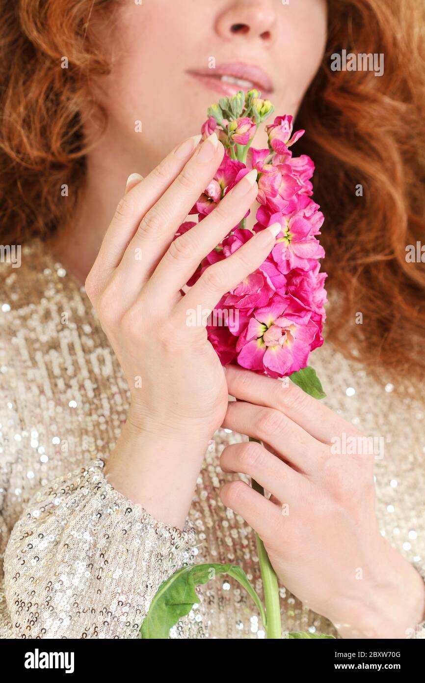 La jeune femme porte une fleur de matthiola rose. De belles mains et de longs ongles naturels. Banque D'Images