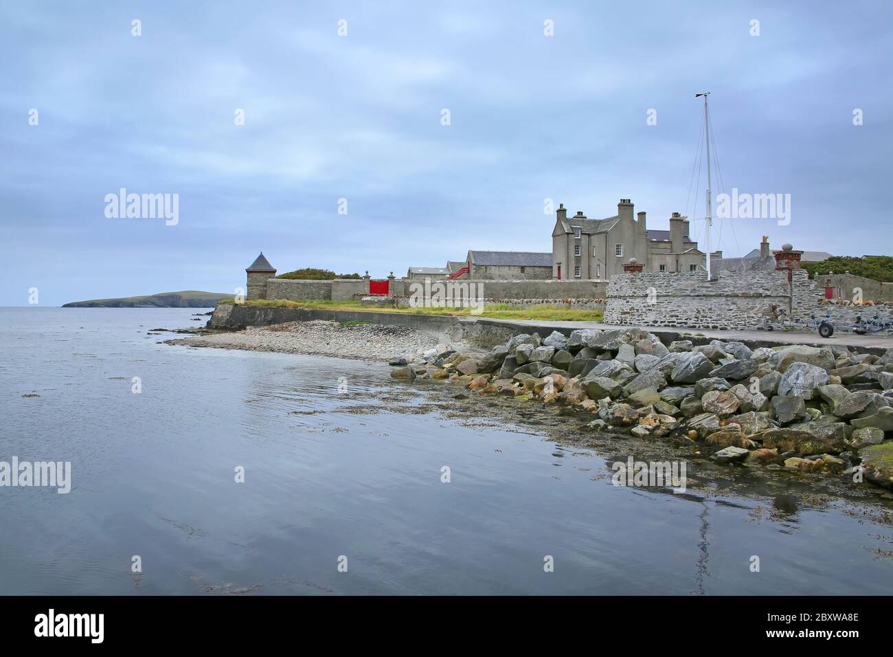 Côte avec galets et rochers et jetée de Sandsayre par une journée d'été grise, Sandwick, îles Shetland, Écosse. Banque D'Images