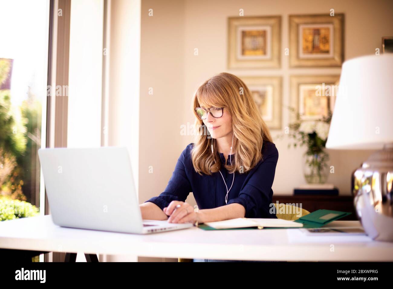 Photo d'une femme d'affaires d'âge moyen utilisant un écouteur, assise derrière son ordinateur portable et ayant des discussions et des réunions en ligne en vidéoconférence. Femme d'affaires Banque D'Images