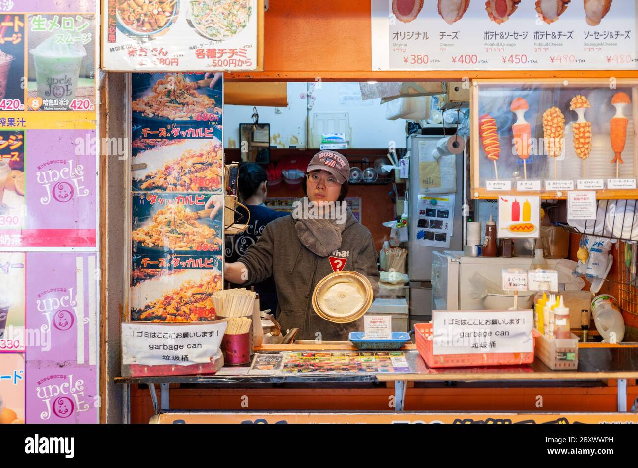 Jeune femme vendeur dans sa cuisine de restauration rapide de son stalle / restaurant à Ameyoko Market, Tokyo, Japon Banque D'Images