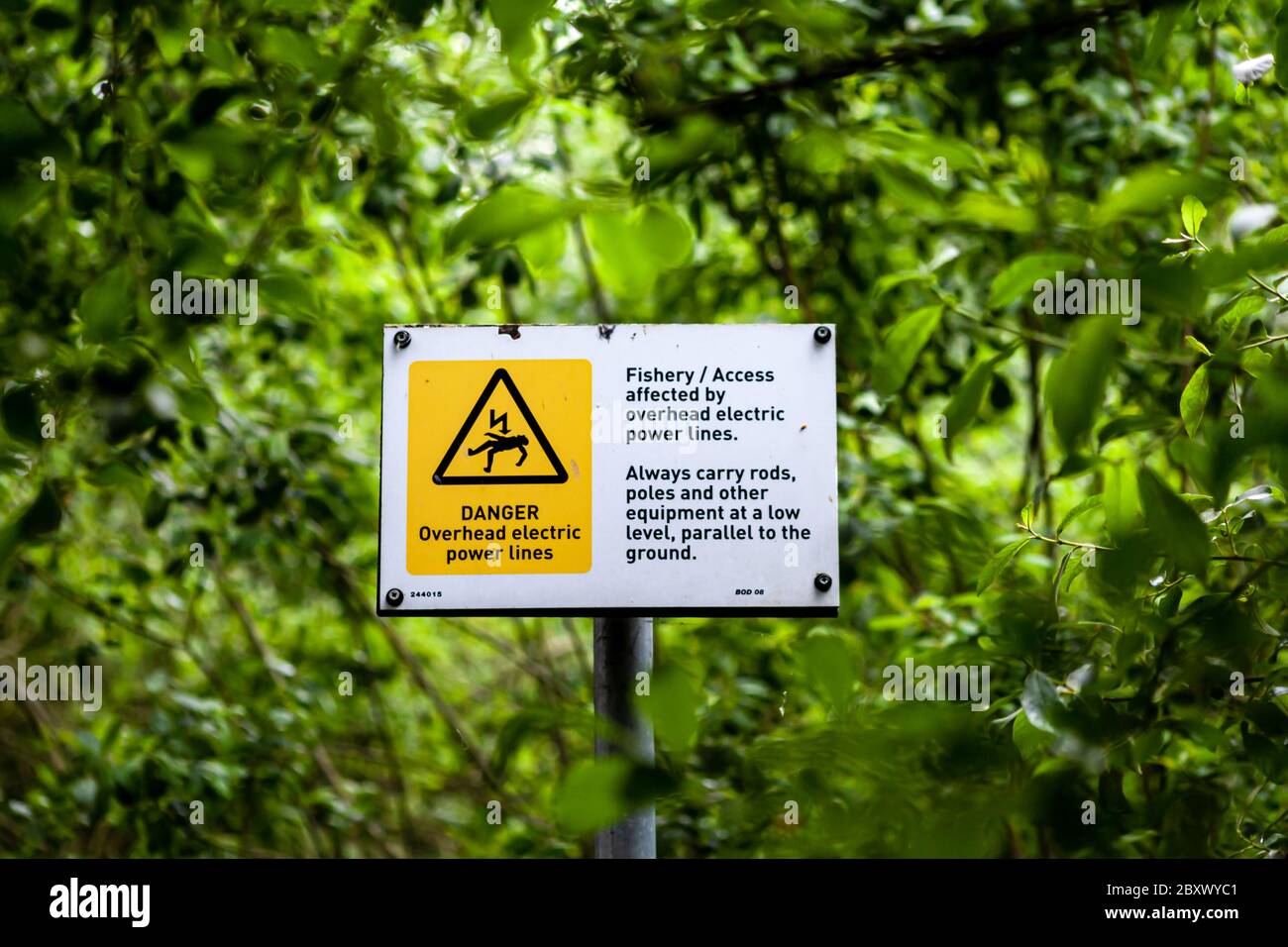 Ces panneaux d'avertissement sont sur un chemin menant à travers un bois à l'étang de pêche local. Ils avertissent des lignes électriques aériennes. Banque D'Images