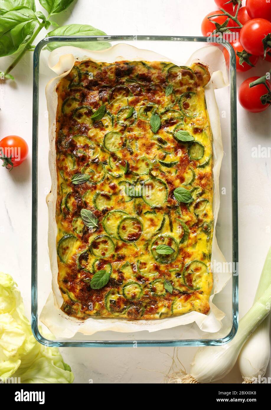 Concept alimentaire. Omelette cuite au four avec courgettes, poireaux et fromage dans un plateau en verre sur fond blanc. Décoration feuilles de menthe. Vue de dessus. Banque D'Images