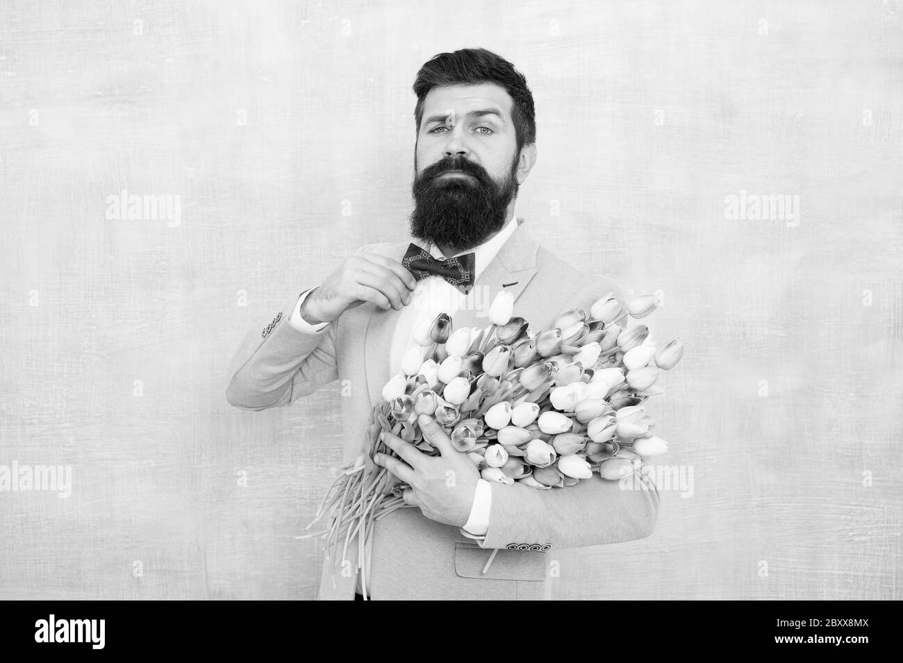 Bonne journée pour femme. L'homme barbu tient des fleurs de printemps. Bouquet de tulipes pour femme. Hipster porter un costume classique et une cravate. Prêt pour la célébration de la journée pour femme. 8 Mars. Vacances internationales pour femmes. Banque D'Images