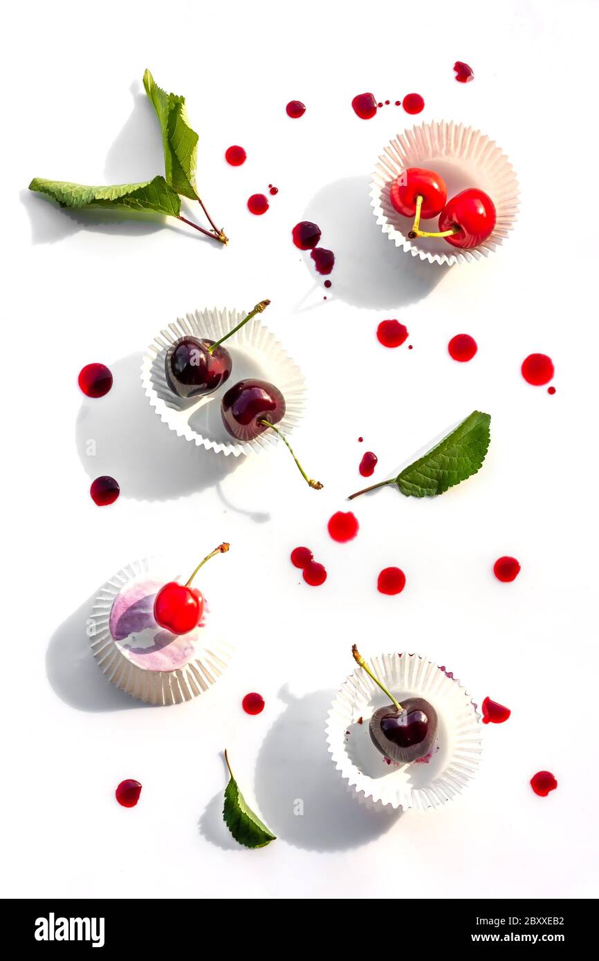 Mise en page estivale créative en cerisier. Fruits mûrs sur fond blanc avec quelques gouttes d'eau et jus de cerise. Vue de dessus Banque D'Images