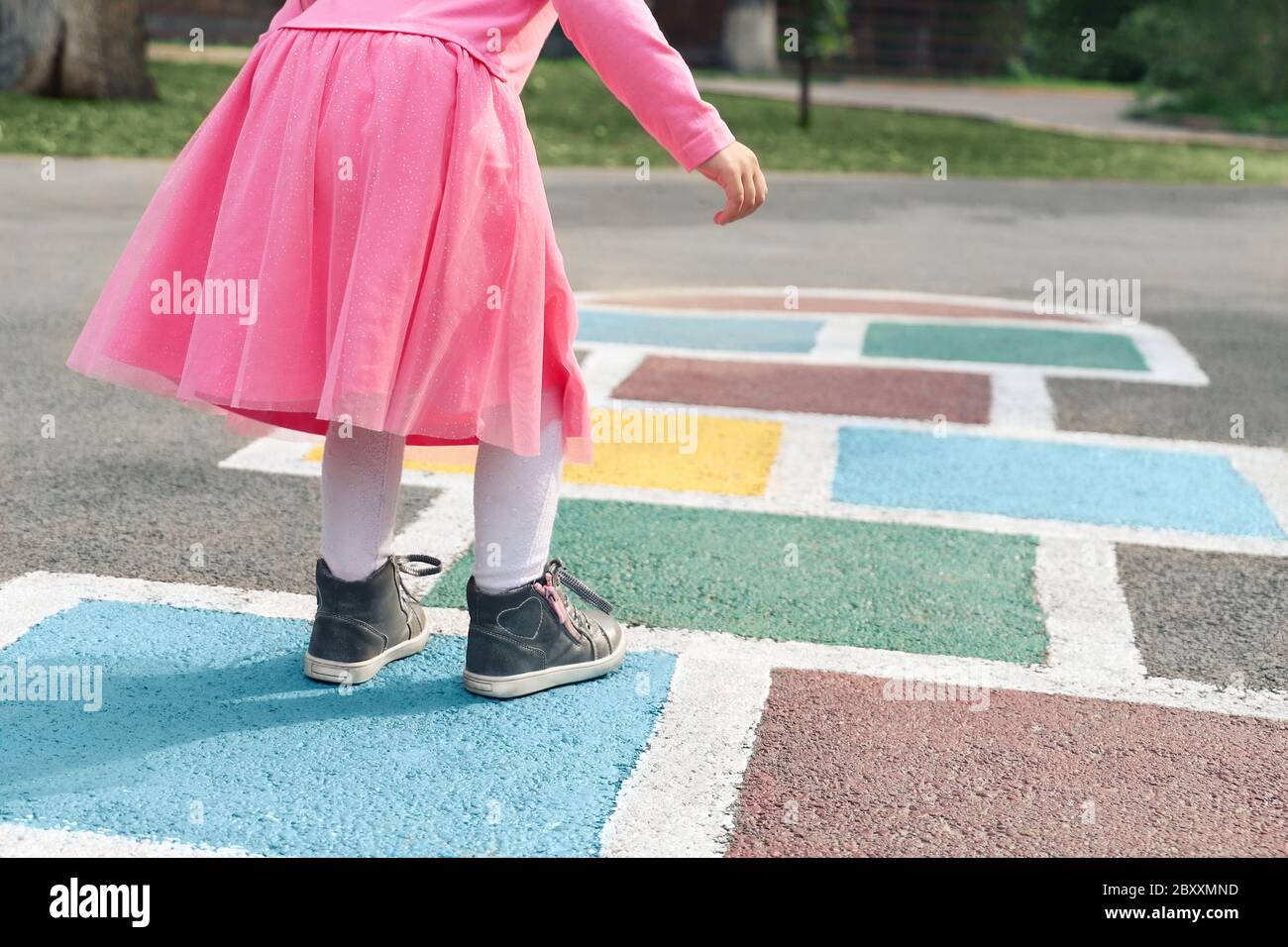 Petite fille dans une robe rose jouant au hopscotch sur le terrain de jeu à l'extérieur, activités de plein air pour enfants Banque D'Images
