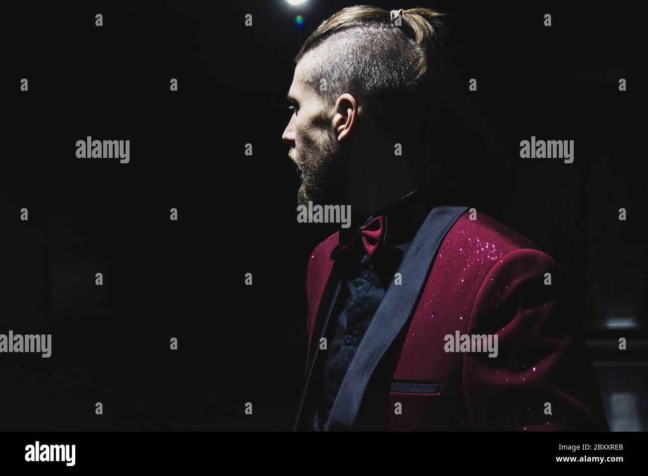 Un homme avec une barbe et une coupe de cheveux élégante a l'air sombre. Veste rouge. Banque D'Images