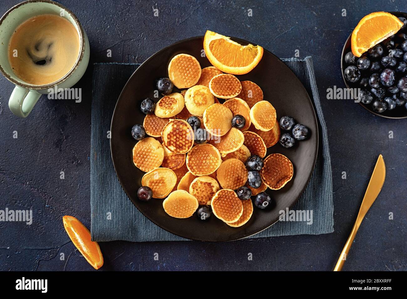 Vue de dessus sur les mini crêpes faites maison dans une assiette noire sur fond bleu Banque D'Images