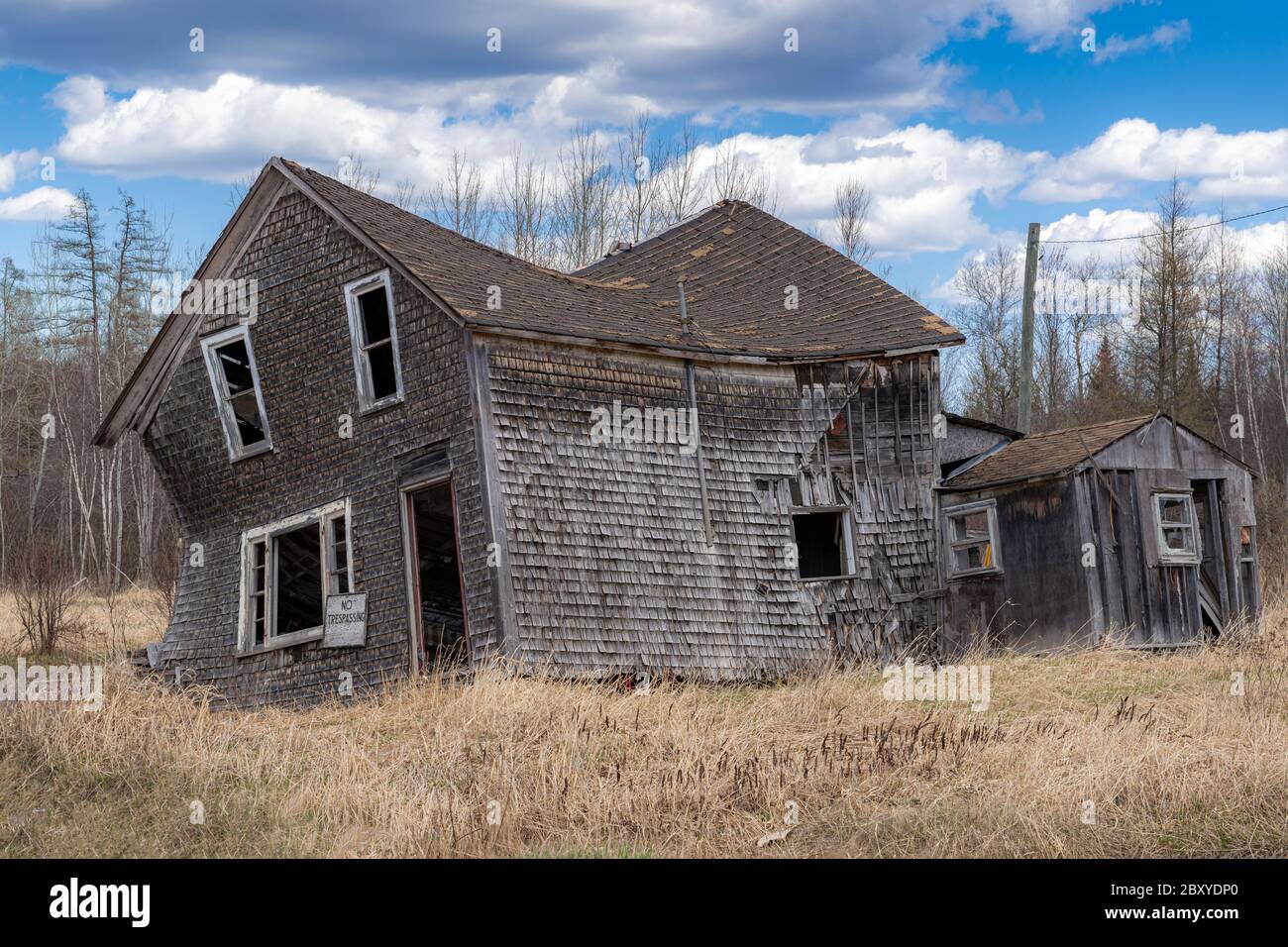 Une maison abandonnée qui s'effondre dans un champ. Fenêtres et porte cassées, pas d'affiche d'intrusion à l'avant. Ciel bleu avec nuages. Banque D'Images
